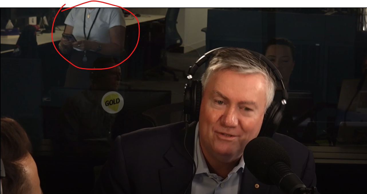 Staff member visible in background reflection during live recording